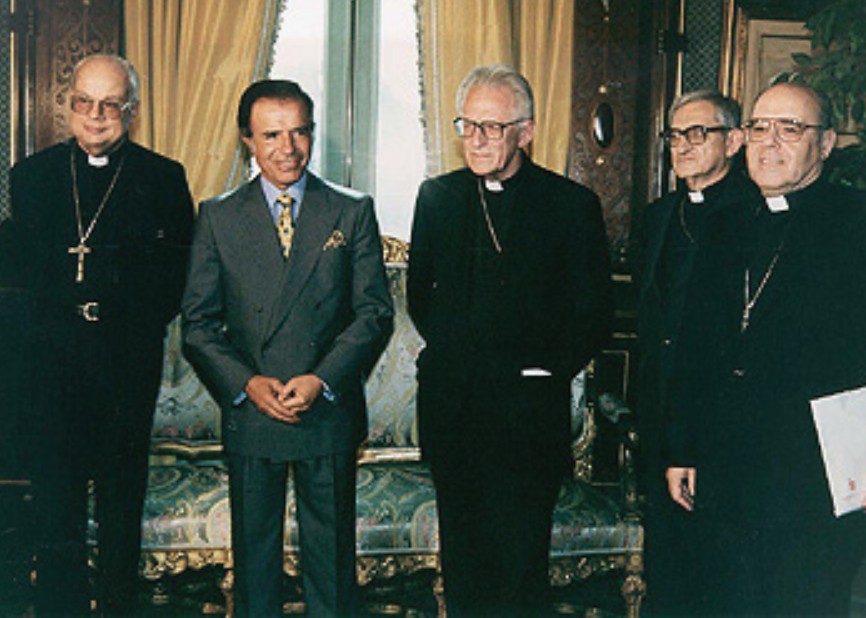 Al centro, en atuendo civil, Carlos Saúl Menem, entonces presidente de Argentina. A la derecha, Estanislao Esteban Karlic, entonces arzobispo de Paraná y presidente de la Conferencia Episcopal Argentina con otros miembros de ese organismo, 1996. Imagen de la Presidencia de Argentina vía Wikimedia. Al centro, en atuendo civil, Carlos Saúl Menem, entonces presidente de Argentina. A la derecha, Estanislao Esteban Karlic, entonces arzobispo de Paraná y presidente de la Conferencia Episcopal Argentina con otros miembros de ese organismo, 1996. Imagen de la Presidencia de Argentina vía Wikimedia.