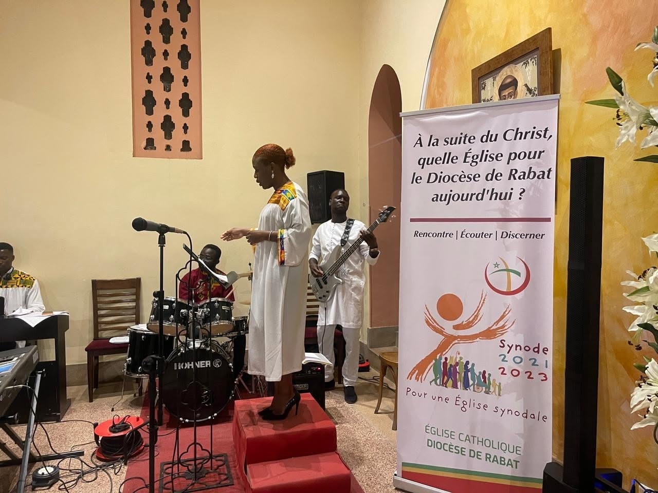 A singer and her band rehearse before a religious service in a Catholic parish in the Archdiocese of Rabat. Notice the French-only lettering to the right of frame asking the faithful to participate in the activities related to the Synod, 2022. From the Archdiocese of Rabat Facebook profile. A singer and her band rehearse before a religious service in a Catholic parish in the Archdiocese of Rabat. Notice the French-only lettering to the right of frame asking the faithful to participate in the activities related to the Synod, 2022. From the Archdiocese of Rabat Facebook profile.